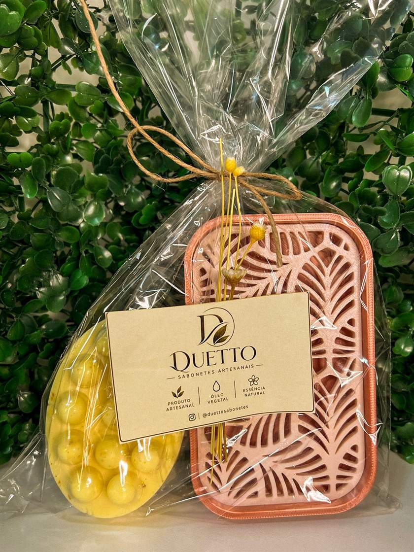 Kit com sabonete massageador amarelo e saboneteira rosa, embalados em celofane com flores secas e etiqueta Duetto